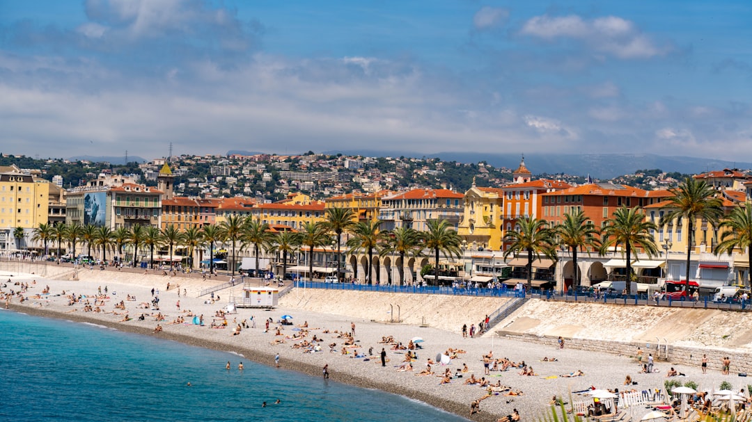 Crowded beach, palm trees, and colorful buildings by blue sea.